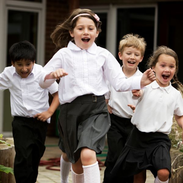 Happy diverse children running outside in school uniforms.