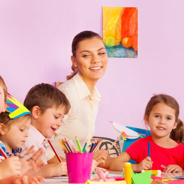 Teacher smiling while children do crafts.