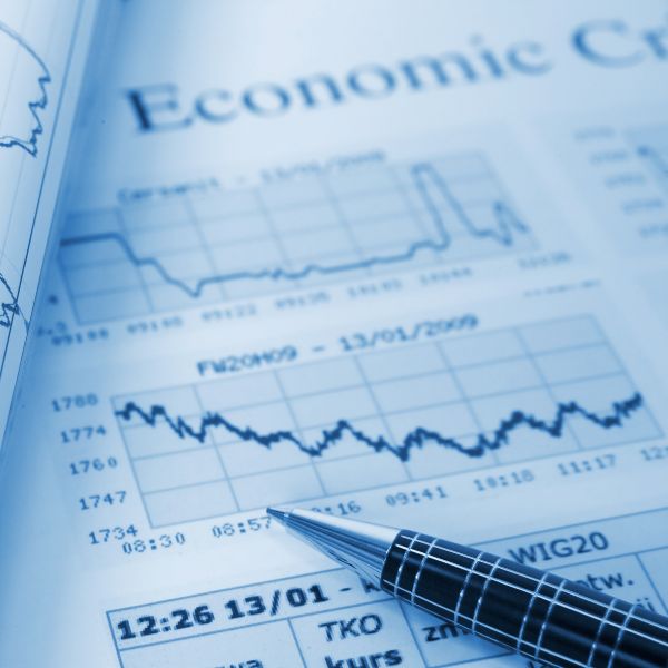 A silver pen rests on a document titled "Economic Crisis" with graphs of a stock market crash.